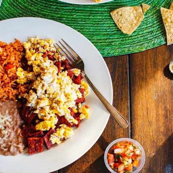 Mexican breakfast plate with scrambled eggs, chorizo, rice, refried beans, and tortilla chips.