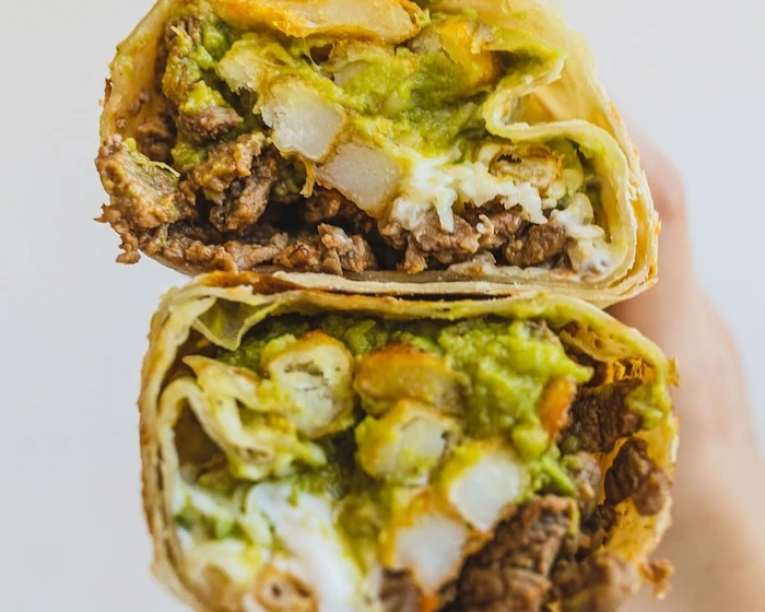 Close-up of a halved burrito filled with steak, crispy fries, creamy guacamole, and cheese. The textures and vibrant colors are appetizing.
